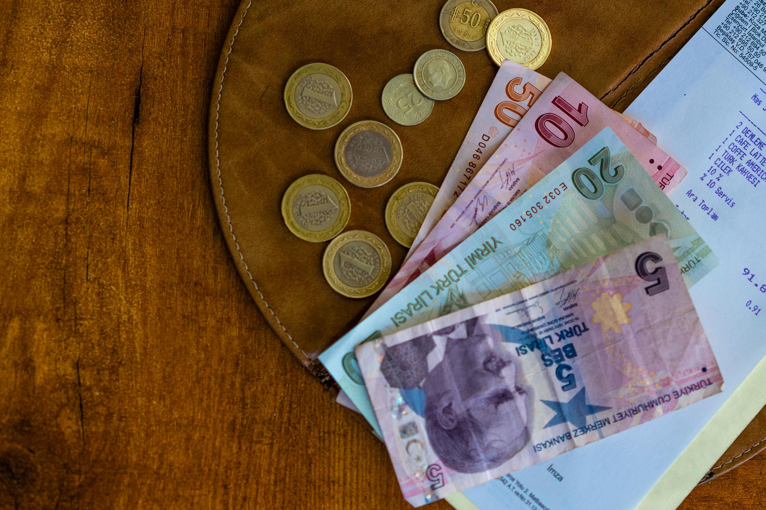 Zbliżenie monet i banknotów liry tureckiej na drewnianej powierzchni obok paragonu. Pieniądze w Turcji.
