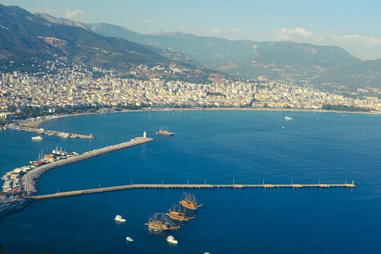 Discover the stunning aerial view of Alanya's vibrant harbor and coastline surrounded by mountains.