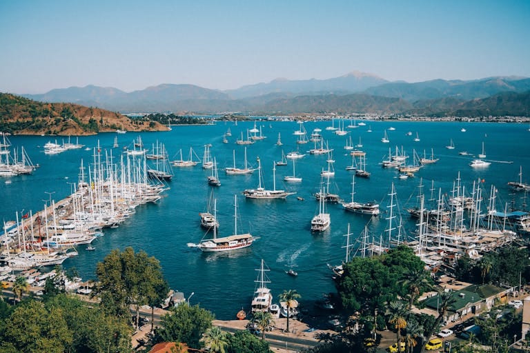 Explore the vibrant Fethiye Marina with dozens of colorful boats docked against a mountain backdrop.