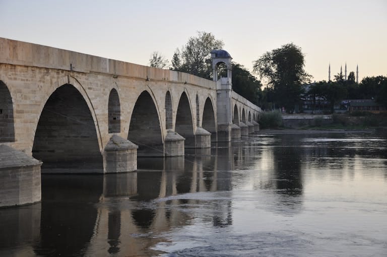 Iconic stone bridge over the Meriç River reflecting in tranquil waters at sunset in Edirne, Turkey.