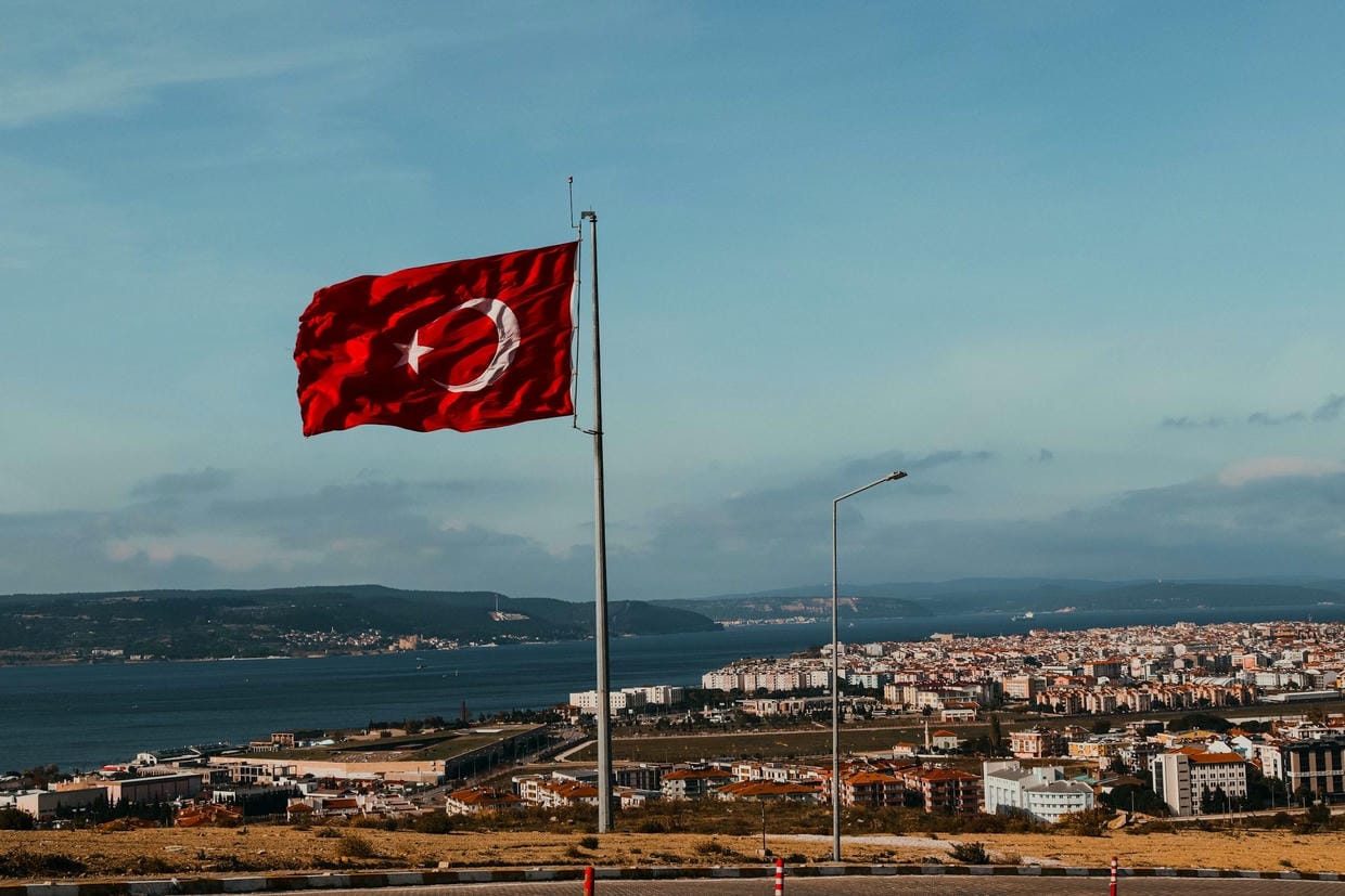 De rode Turkse vlag wappert op een heldere dag boven een kuststedelijk landschap in Turkije.